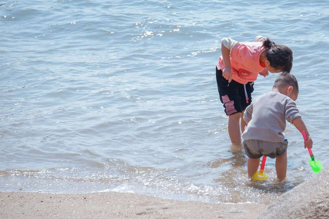 uomo in camicia rossa che trasporta bambino in camicia bianca sulla spiaggia puzzle online