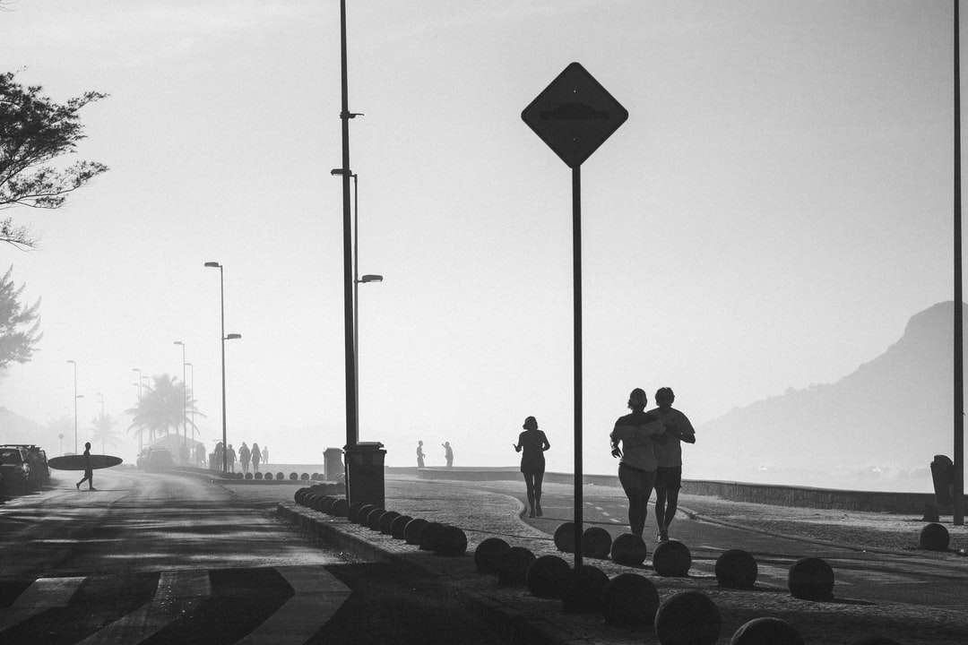 Foto en escala de grises de personas caminando en la acera cerca del cuerpo rompecabezas en línea