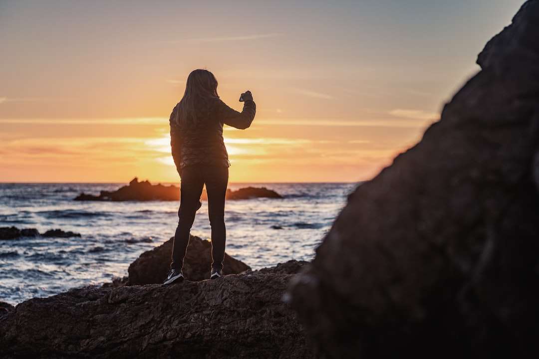 Silhouette des Mannes, der auf Felsen nahe dem Gewässer steht Puzzlespiel online