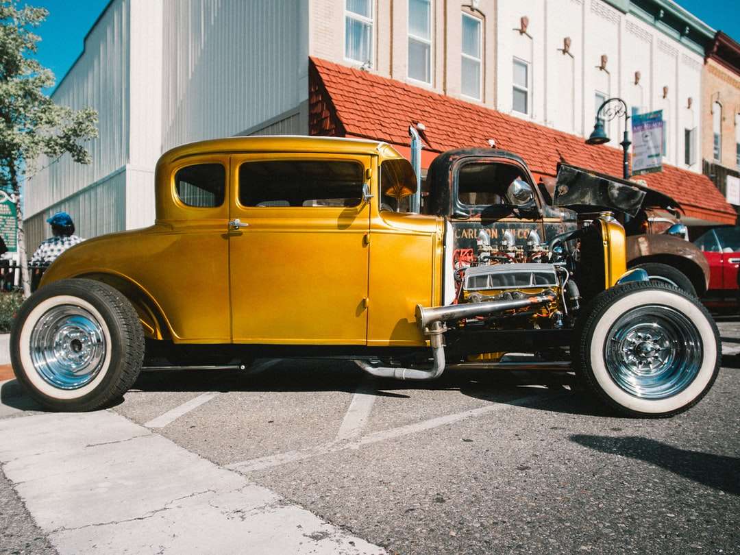gelbes altes Auto, das nahe weißem Gebäude geparkt wird Online-Puzzle