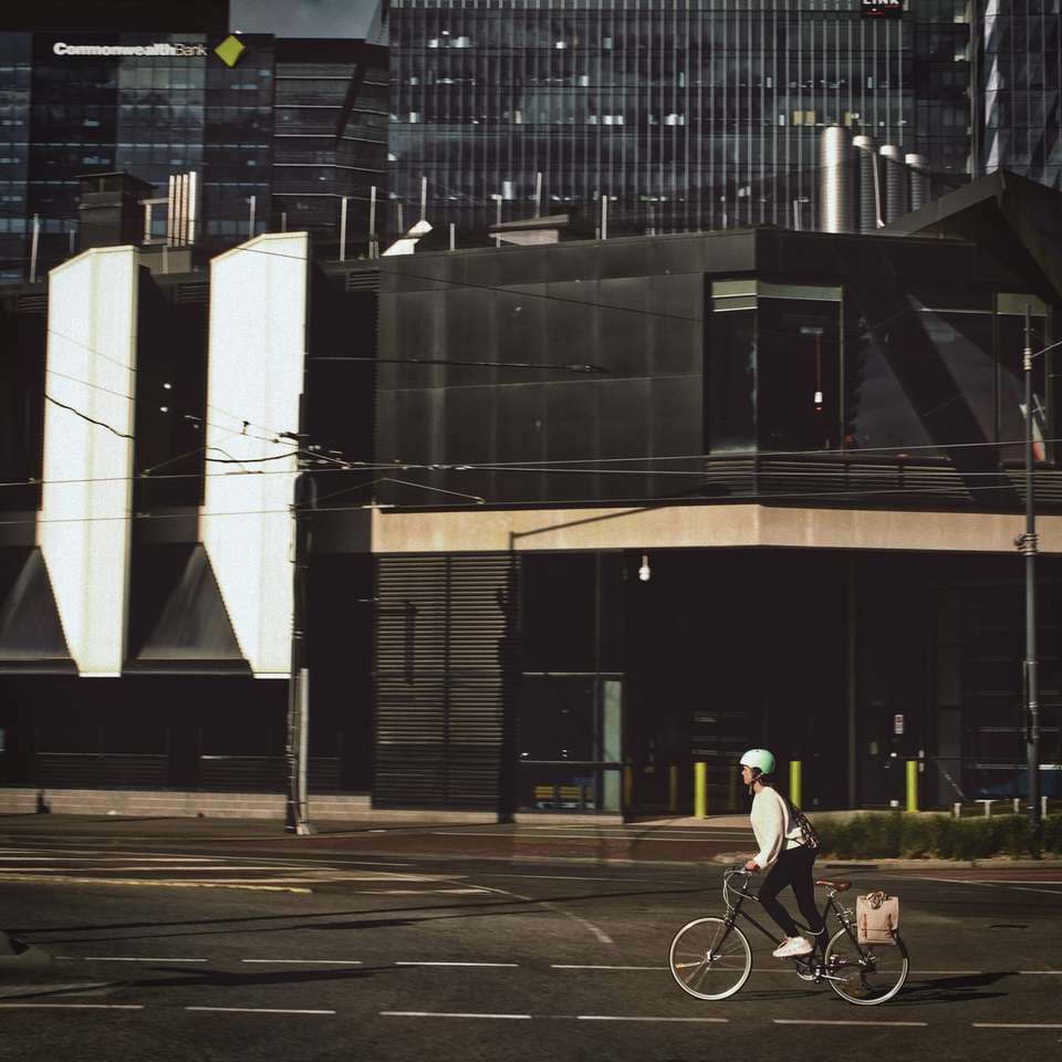 мъж в черна риза, каране на велосипед по пътя близо до сградата онлайн пъзел