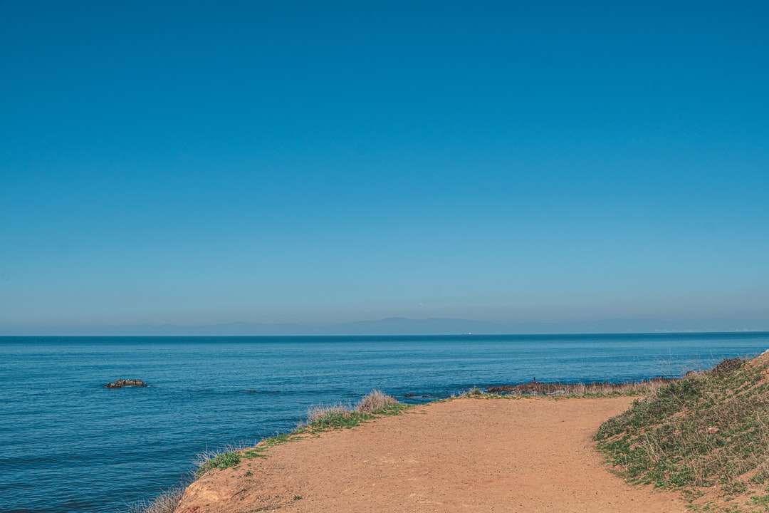 nisip maro lângă mare albastră sub cer albastru în timpul zilei puzzle online
