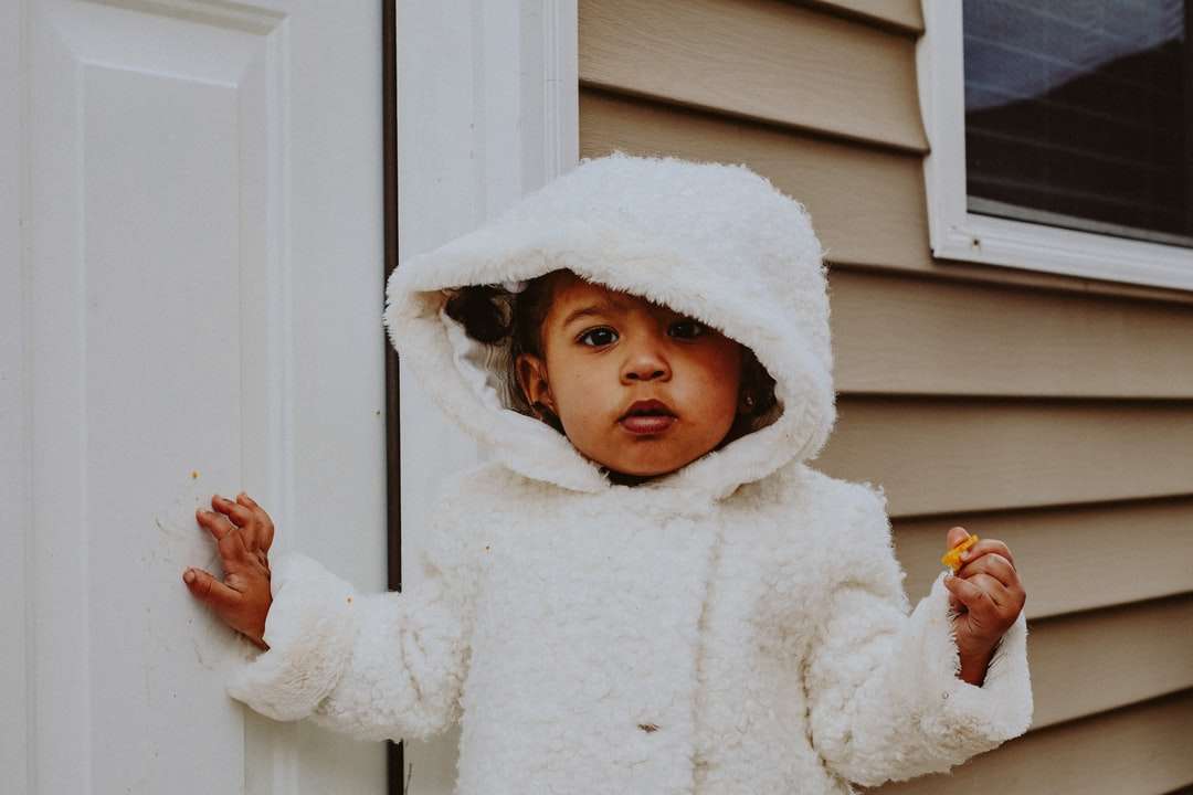 ребенок в белом зимнем пальто стоит у белой деревянной двери пазл онлайн