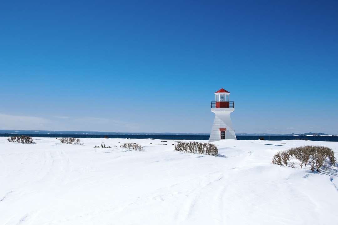 white and red lighthouse on snow covered ground online puzzle
