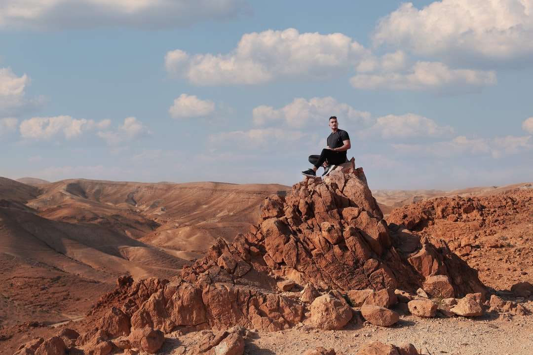 uomo in giacca nera seduto sulla formazione rocciosa durante il giorno puzzle online