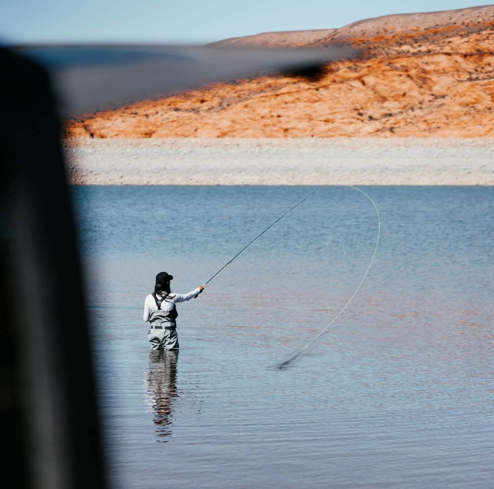 Hombre de chaqueta negra pescando en el mar durante el día rompecabezas