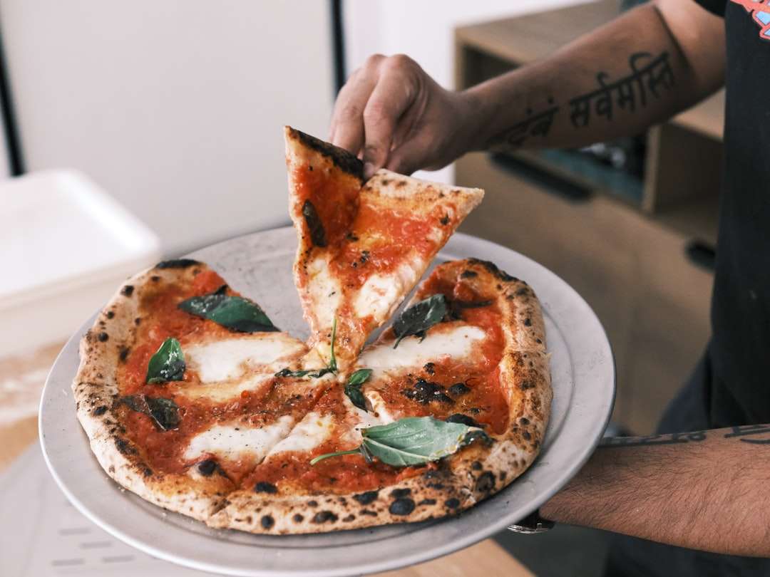 Person, die geschnittene Pizza auf weißer Keramikplatte hält Online-Puzzle