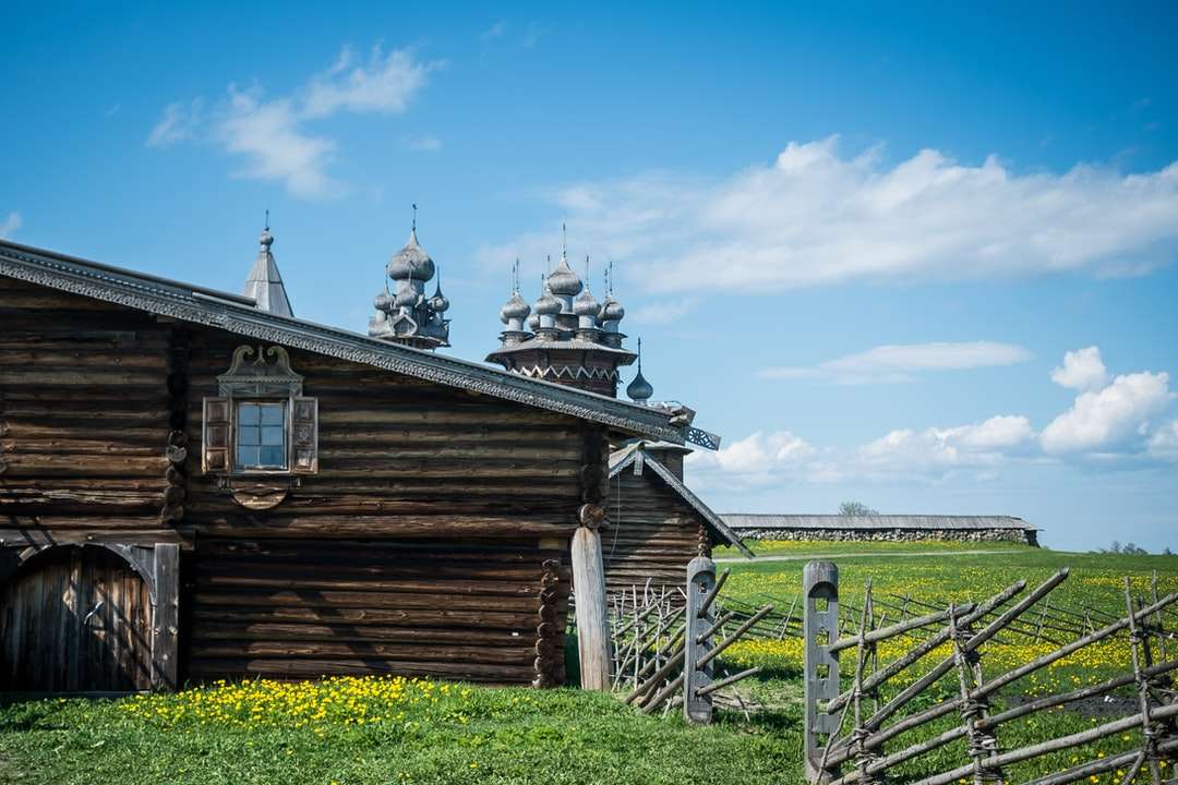кафява дървена къща на зелено тревно поле под синьо небе онлайн пъзел