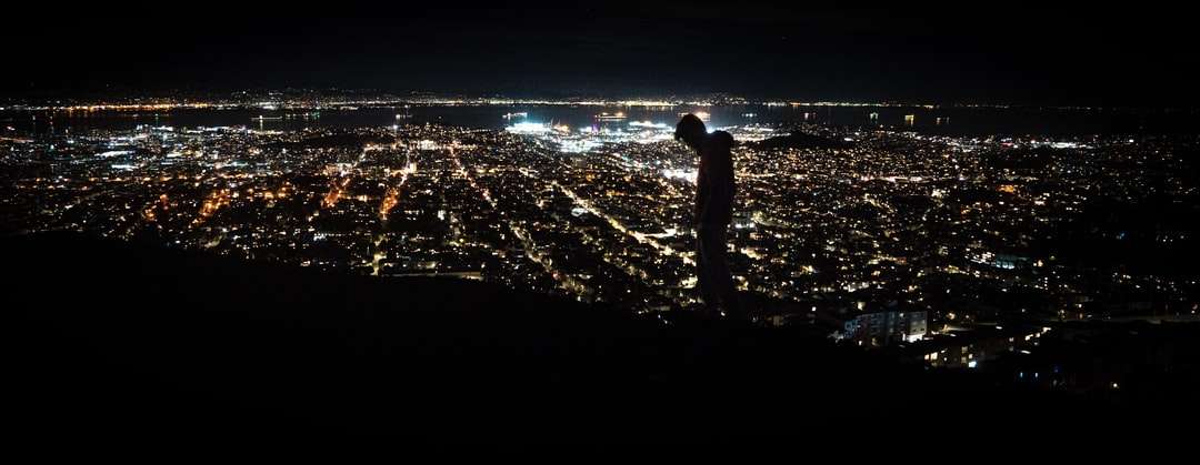 Mann, der auf dem Boden steht und die Lichter der Stadt betrachtet Online-Puzzle