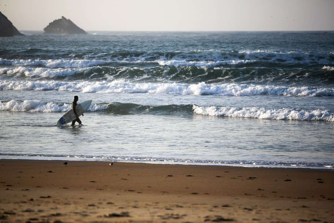 мъж в черен мокър костюм, сърфиращ на морски вълни през деня онлайн пъзел