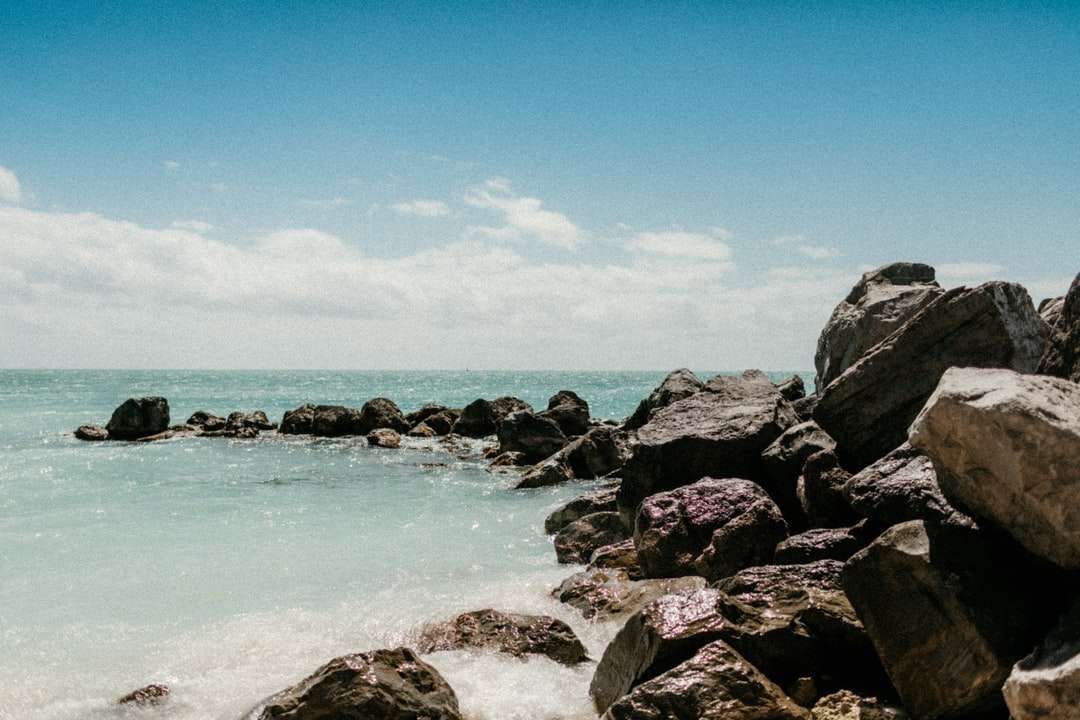 Orilla rocosa con rocas y agua del océano bajo un cielo azul rompecabezas en línea