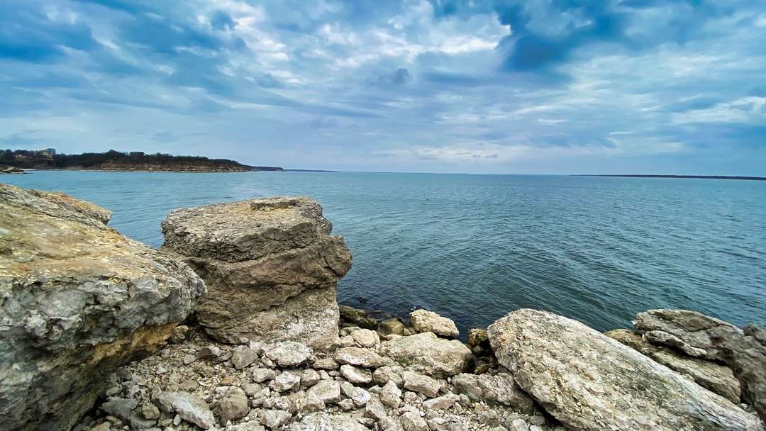 grijze en bruine rotsen dichtbij waterlichaam onder blauwe hemel online puzzel