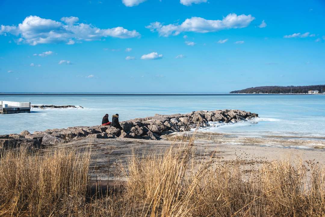 Човек седи на скала близо до морето под синьо небе през деня онлайн пъзел