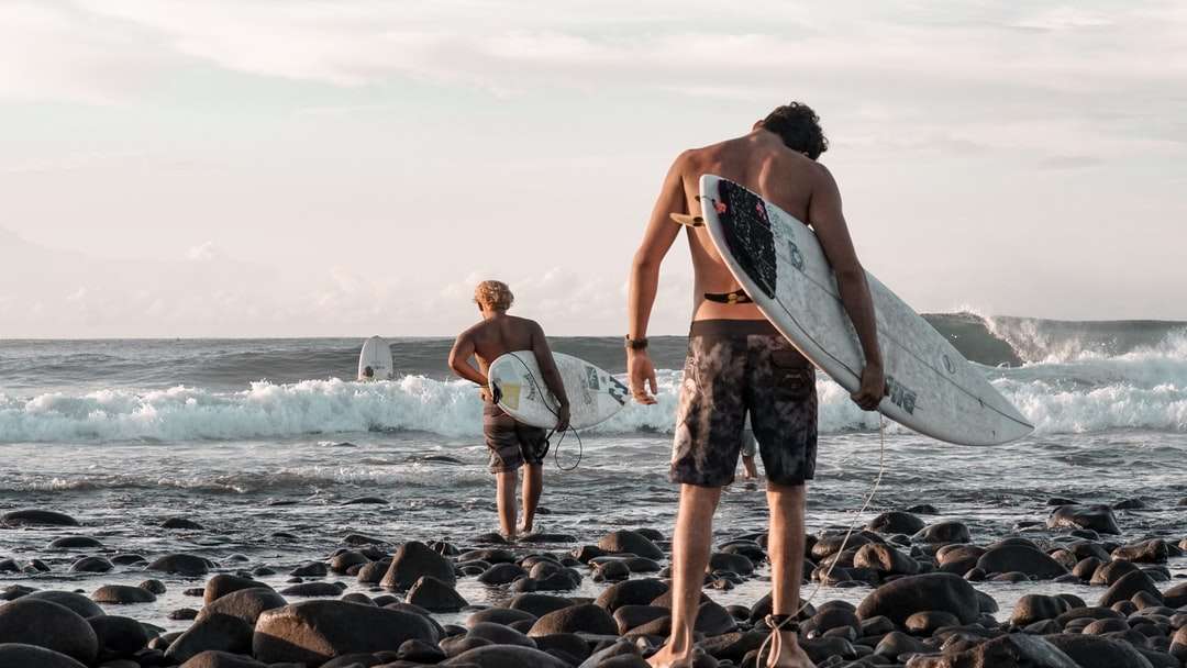 2 donne che tengono il surf in piedi sulla riva rocciosa puzzle online