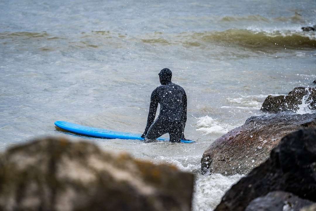 Mann im schwarzen nassen Anzug, der blaues Surfbrett hält Online-Puzzle