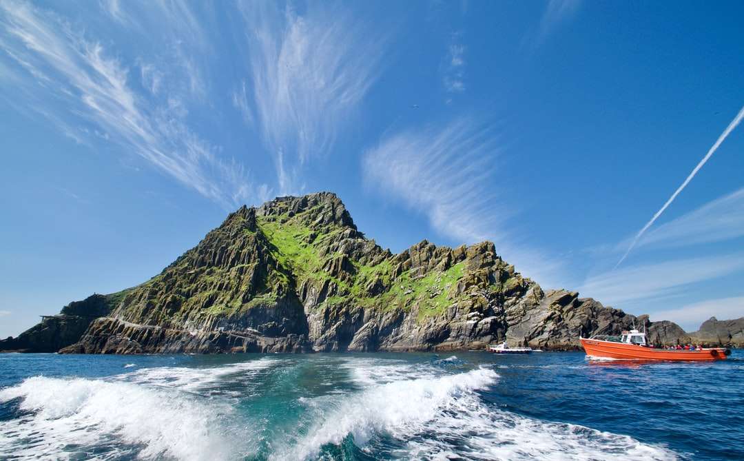 Grüne und braune Felsformation auf Meer unter blauem Himmel Puzzlespiel online