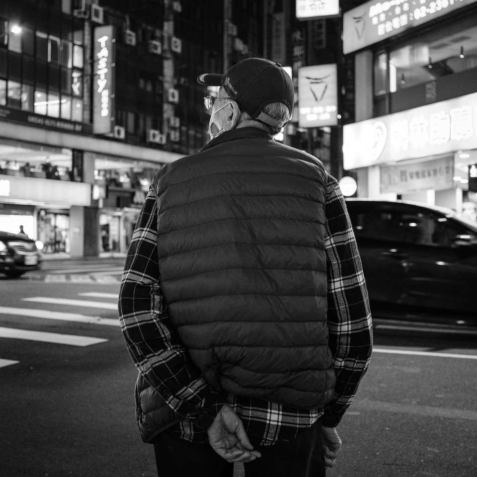 Man i svart och vit plädjacka som står på trottoaren pussel på nätet