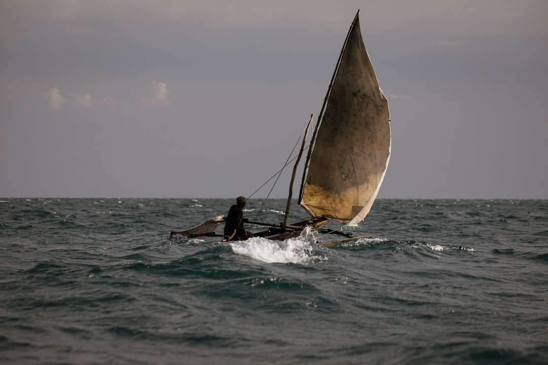 Persona in tuta bagnata nera a cavallo sulla barca a vela sul mare puzzle online