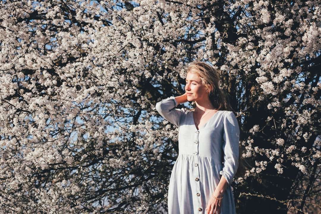 Frau im weißen Kleid, das nahe weißen Blumen steht Puzzlespiel online