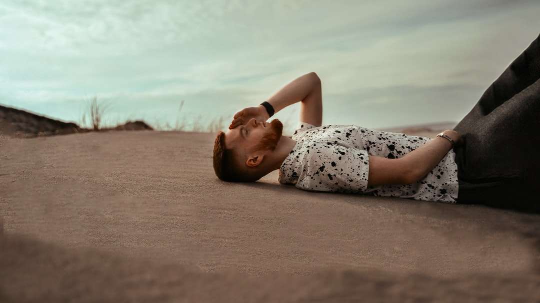 Nő fehér és fekete virágos ruhában fekszik a barna homok online puzzle