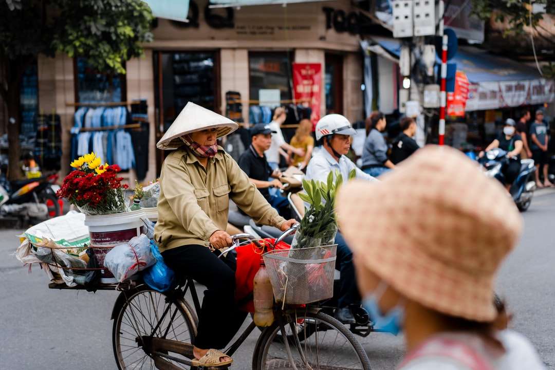 Frau in der braunen Jacke und der weißen Hut, der auf schwarzem Fahrrad reitet Online-Puzzle