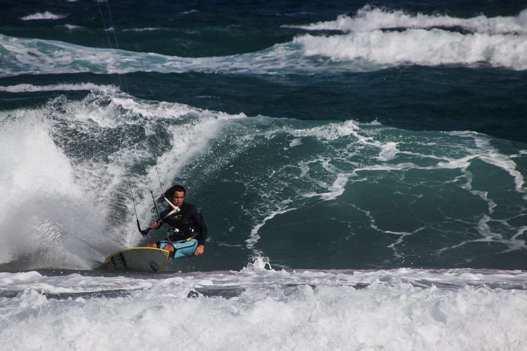 Man i svart våt kostym Ridning gul surfbräda på havsvågor Pussel online