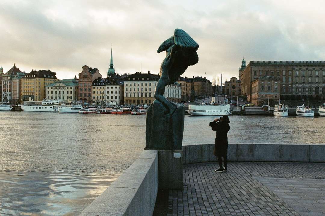 Statue des Mannes, der Regenschirm nahe Körper des Wassers hält Online-Puzzle