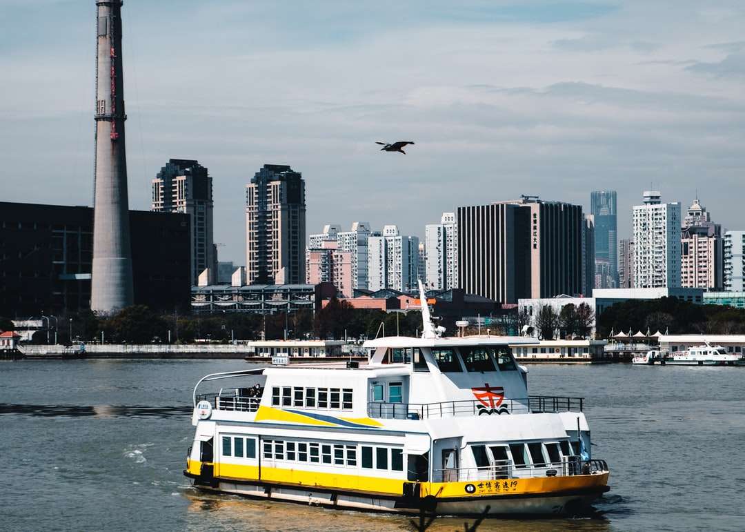 Barco branco e amarelo na água perto de edifícios da cidade quebra-cabeças online