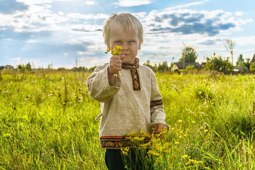 Junge in der grauen Strickjacke, die auf grüner Grasfeld steht Puzzlespiel online