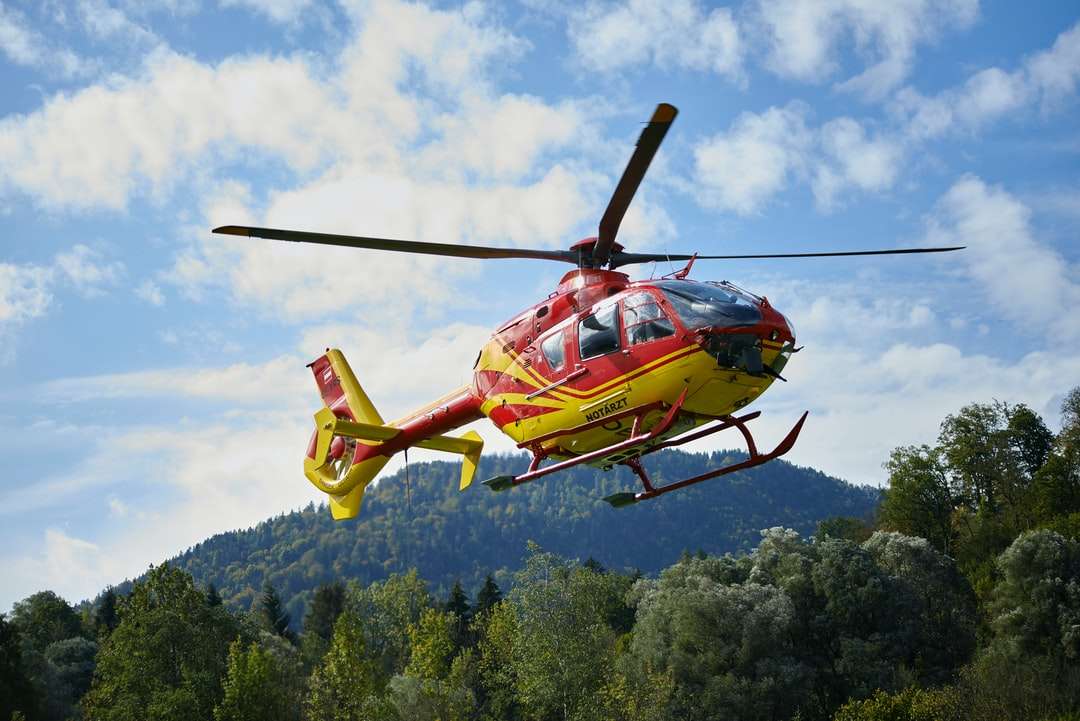 red and yellow helicopter flying over green trees jigsaw puzzle online