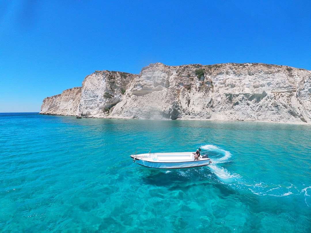 Бяла и синя лодка на синьо море близо до сива скална планина онлайн пъзел