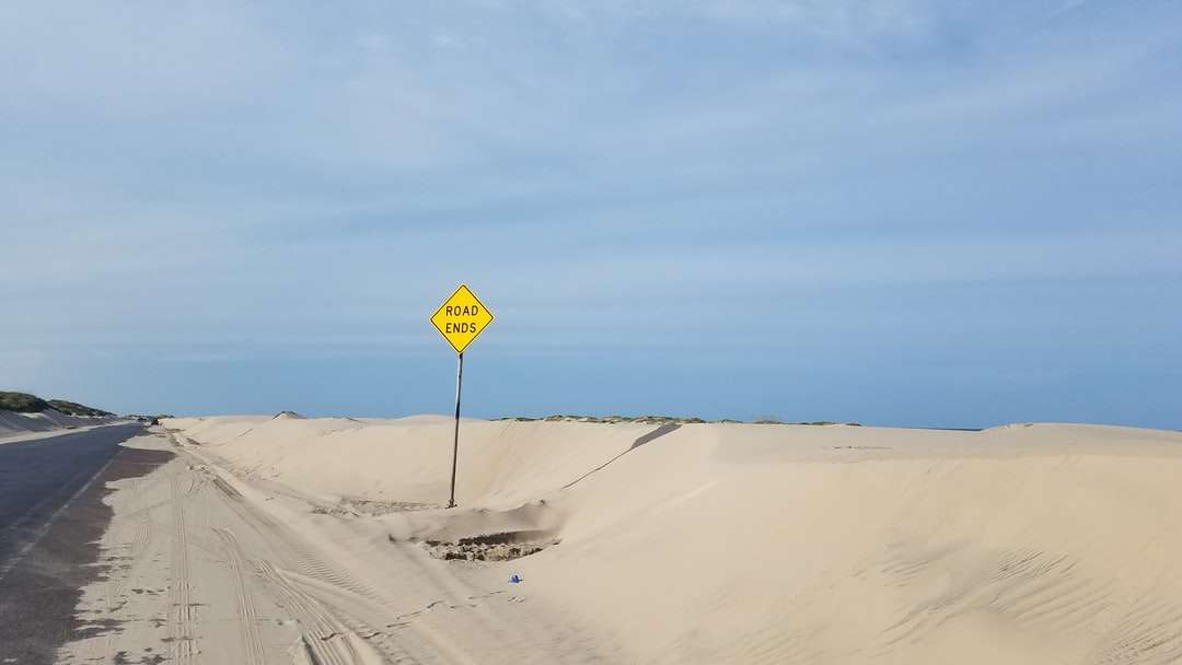 желтый и черный дорожный знак на белом песке пазл онлайн