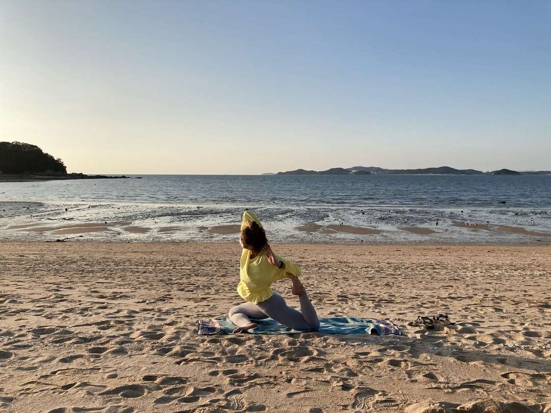 Frau im gelben Kleid, das am Strand an der Tagesuhr am Strand sitzt Online-Puzzle