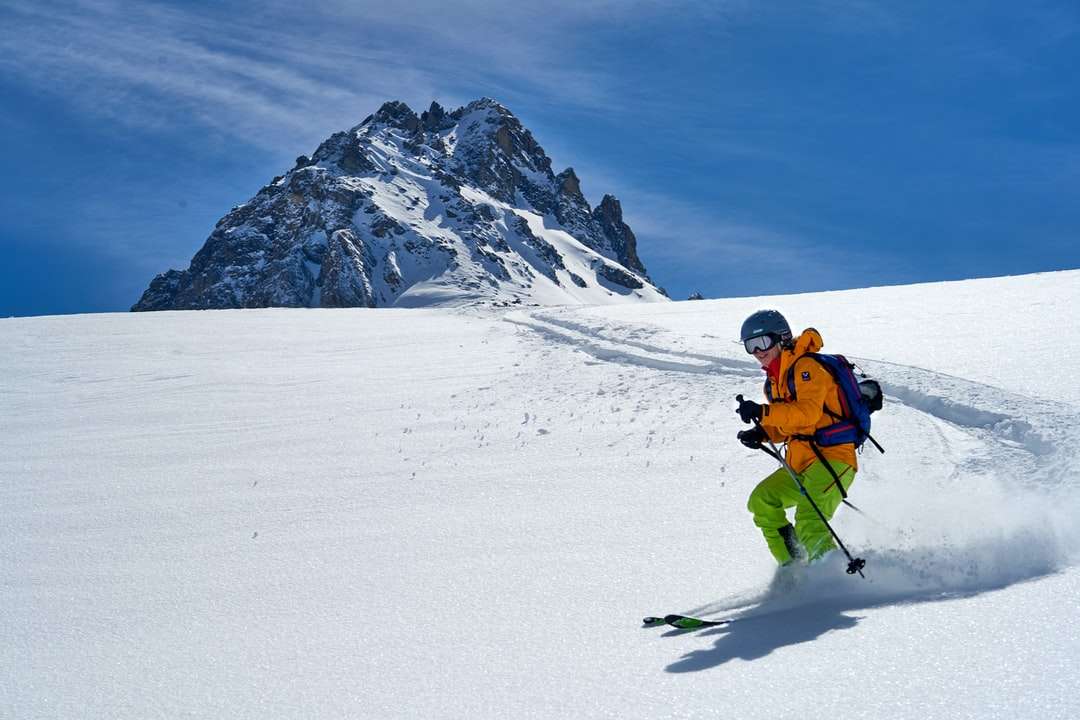 Hombre en chaqueta naranja y pantalones negros montando cuchillas de esquí rompecabezas en línea