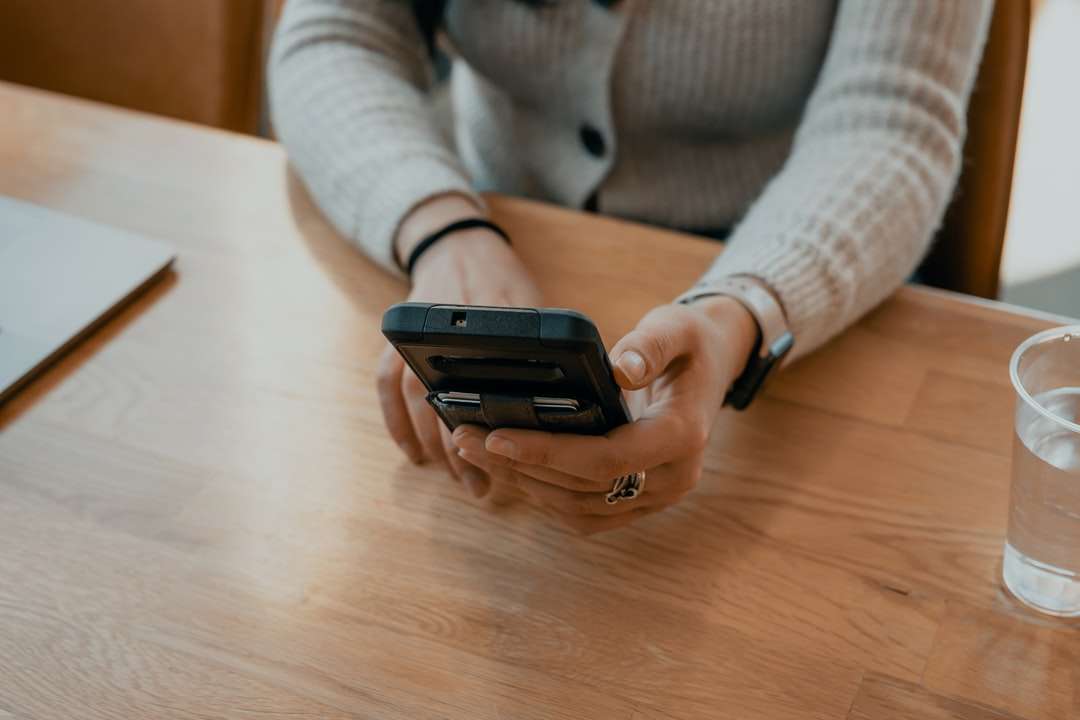 Žena v bílém svetru drží černý smartphone skládačky online