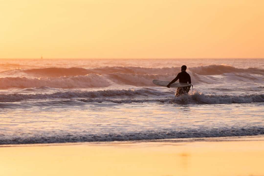 Ο άνθρωπος σερφάρει σε κύματα της θάλασσας κατά τη διάρκεια του ηλιοβασιλέματος online παζλ