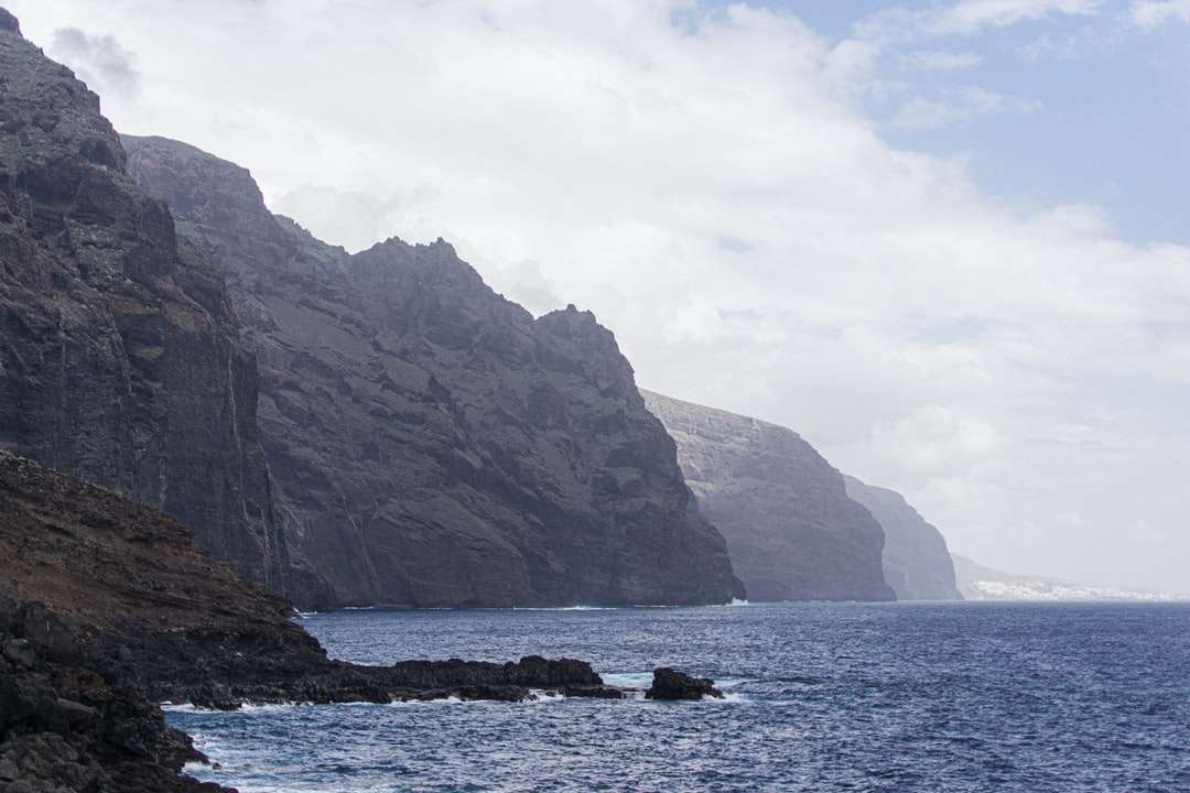 Montanha rochosa marrom ao lado do mar durante o dia puzzle online