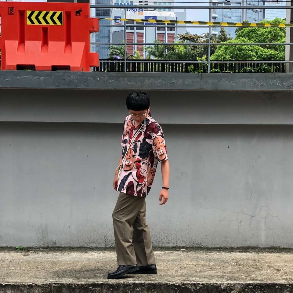 Човек в кафяви панталони стои близо до червена и бяла сграда онлайн пъзел
