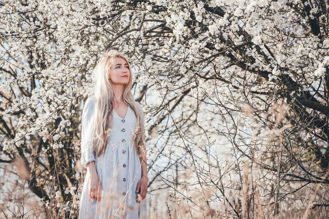 Kvinna i vit klänning som står nära vitt lövträd Pussel online