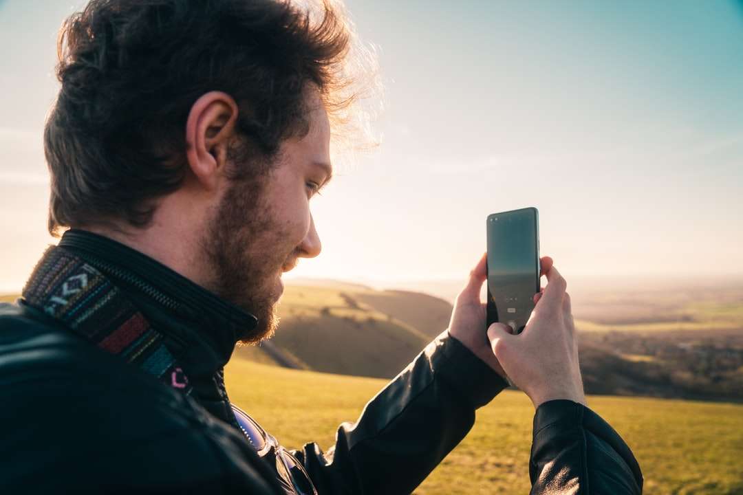 Az ember fekete kabátban tartja az iPhone-t napközben kirakós online