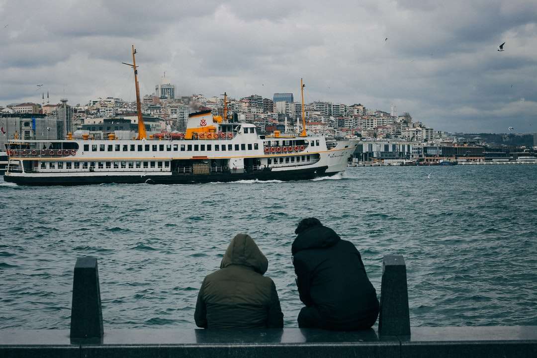 Uomo in felpa con cappuccio nero seduto sul bordo della barca guardando puzzle online