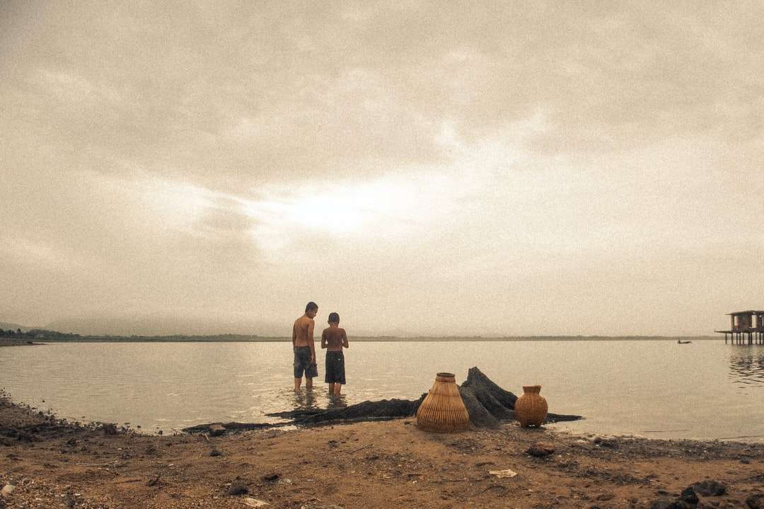Persone in piedi sulla sabbia marrone vicino al corpo dell'acqua puzzle online