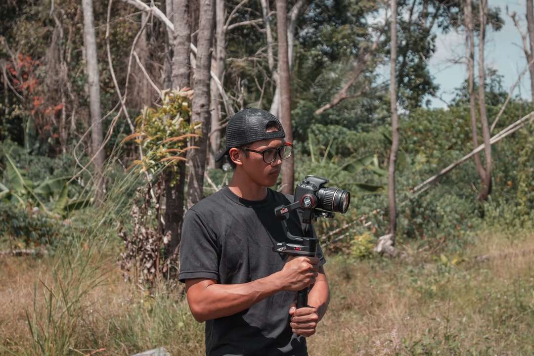Ο άνθρωπος σε μαύρο μπλουζάκι του πληρώματος που κρατά μαύρο κάμερα DSLR online παζλ