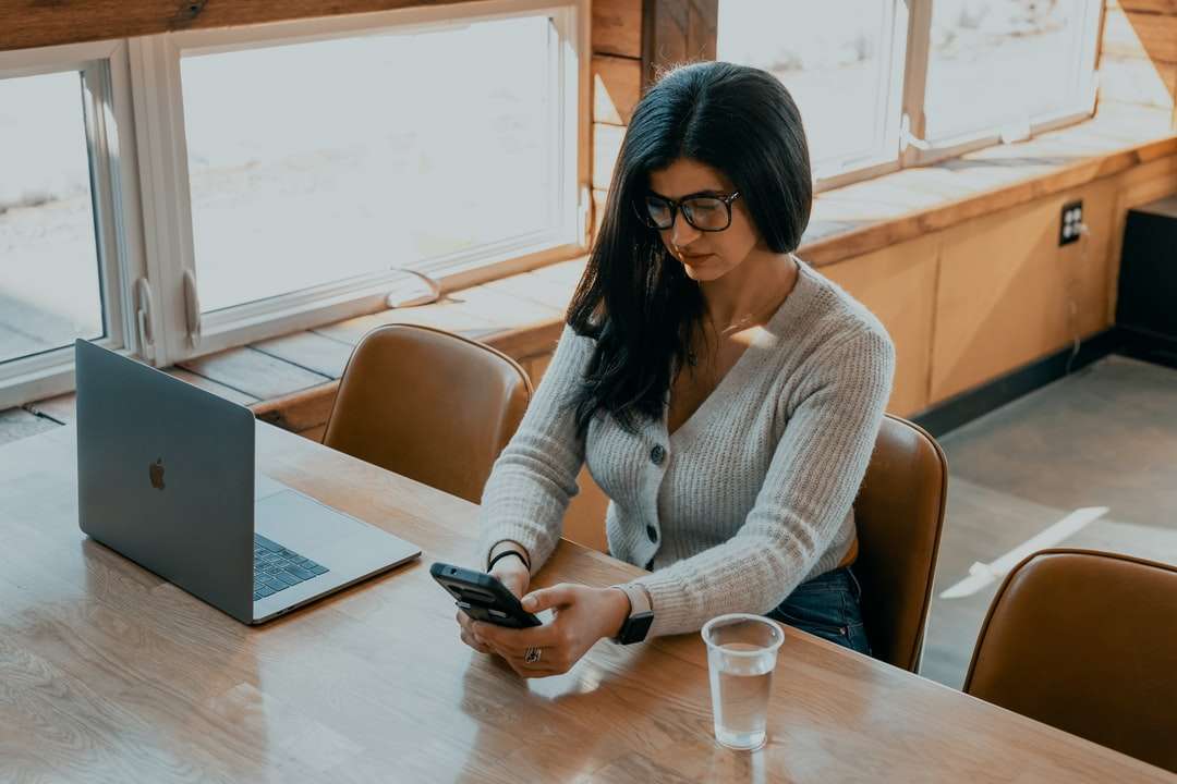 Žena v bílém svetru sedí na židli drží smartphone skládačky online