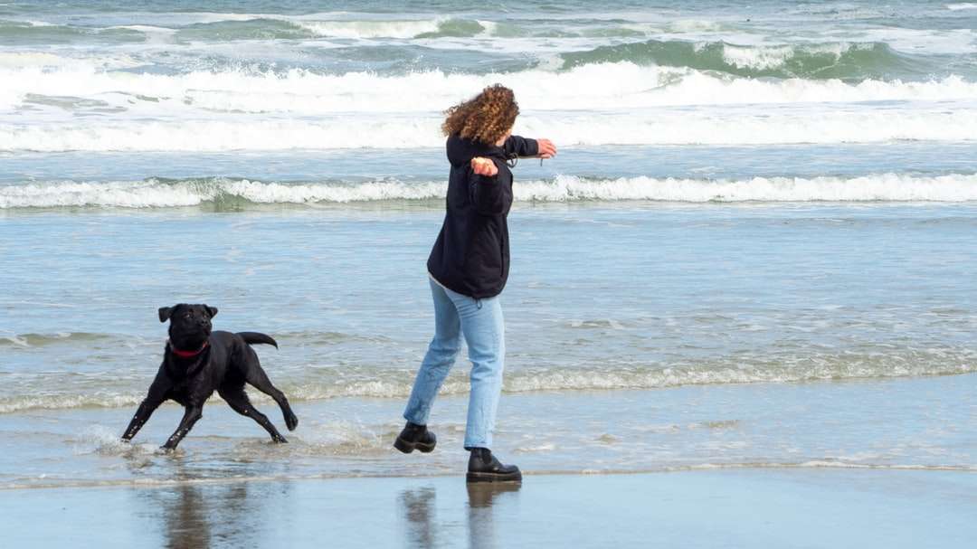 Kvinna i svart jacka och vita byxor som går på stranden Pussel online