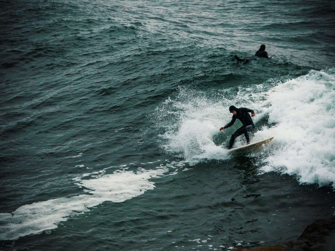 Homme en costume mouillé rouge et noir surfer sur les vagues de la mer puzzle en ligne