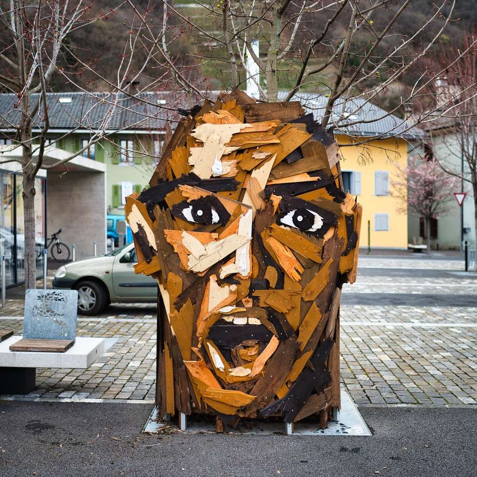 Braune hölzerne menschliche Gesicht geschnitzte Statue auf grauer Betonstraße Puzzlespiel online