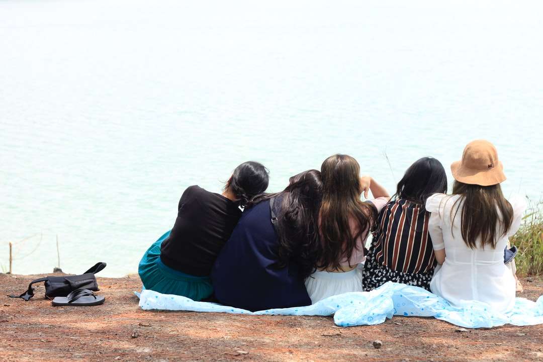 3 Frauen, die auf braunem Sand nahe Körper des Wassers sitzen Puzzlespiel online