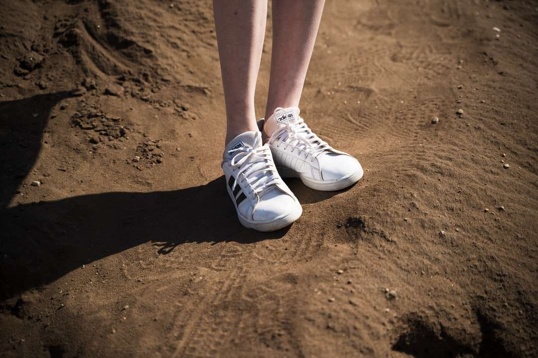 Person som bär vita låga sneakers som står på brun sand Pussel online