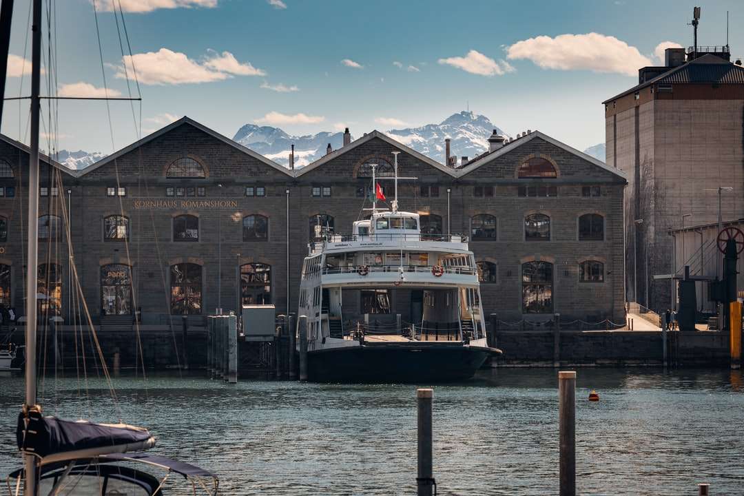 Bílá a černá loď na vodě poblíž brown betonové budovy skládačky online